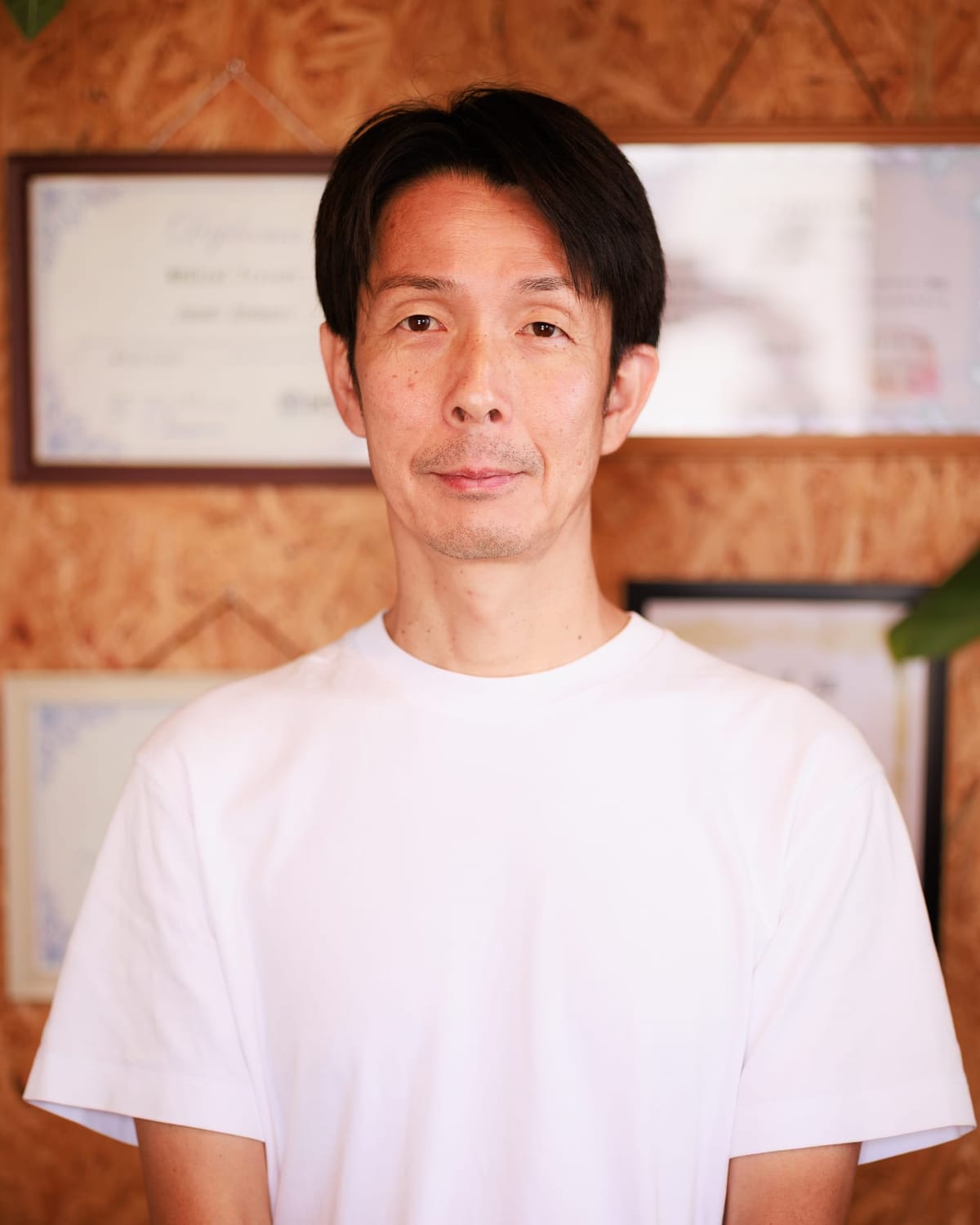 サロンの木の壁を背に立つ、ito relaxation & photo の施術者 鈴木英典